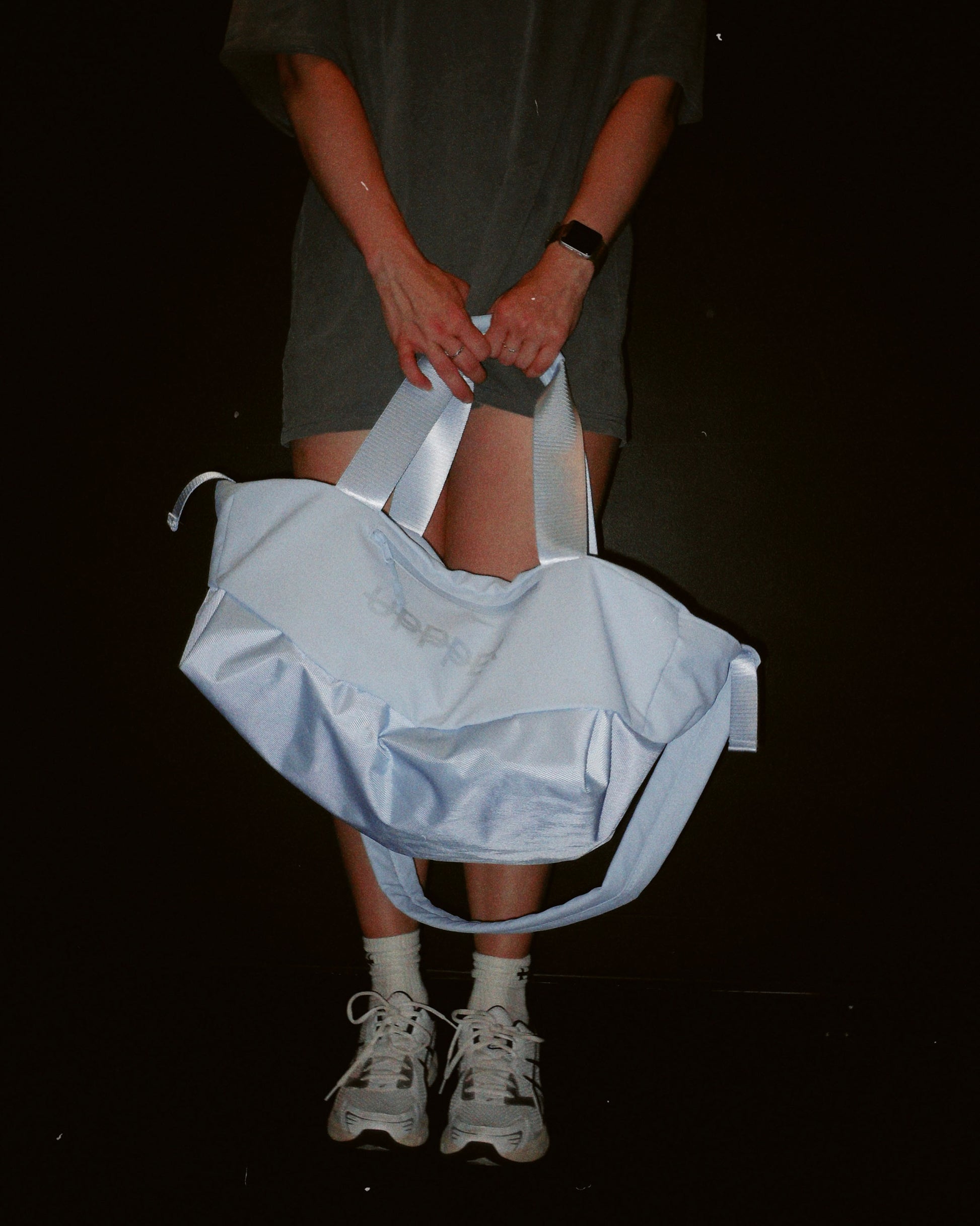 person holding a light blue uppper gym bag on a black background