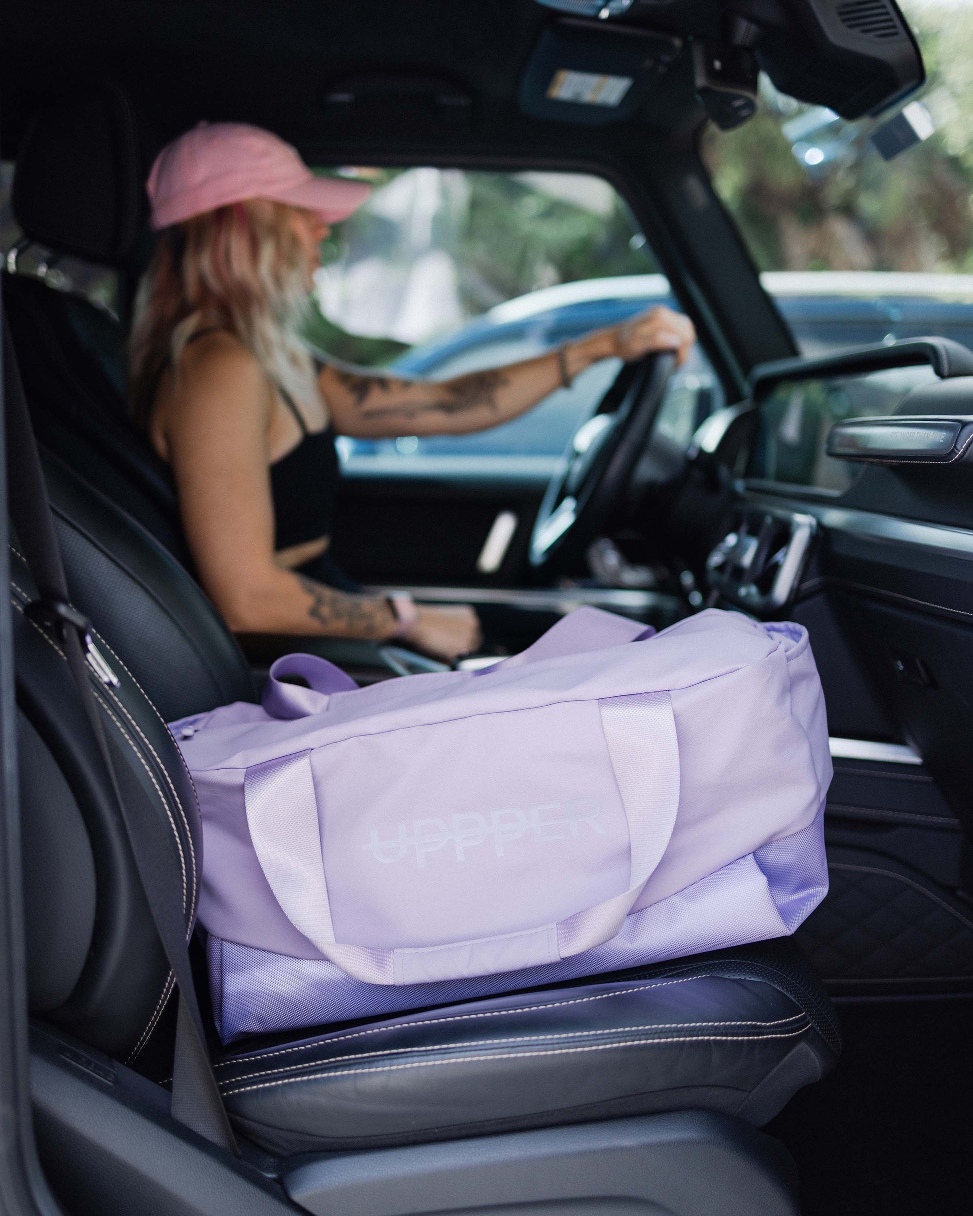person sitting in a car with a purple uppper duffel gym bag on the seat