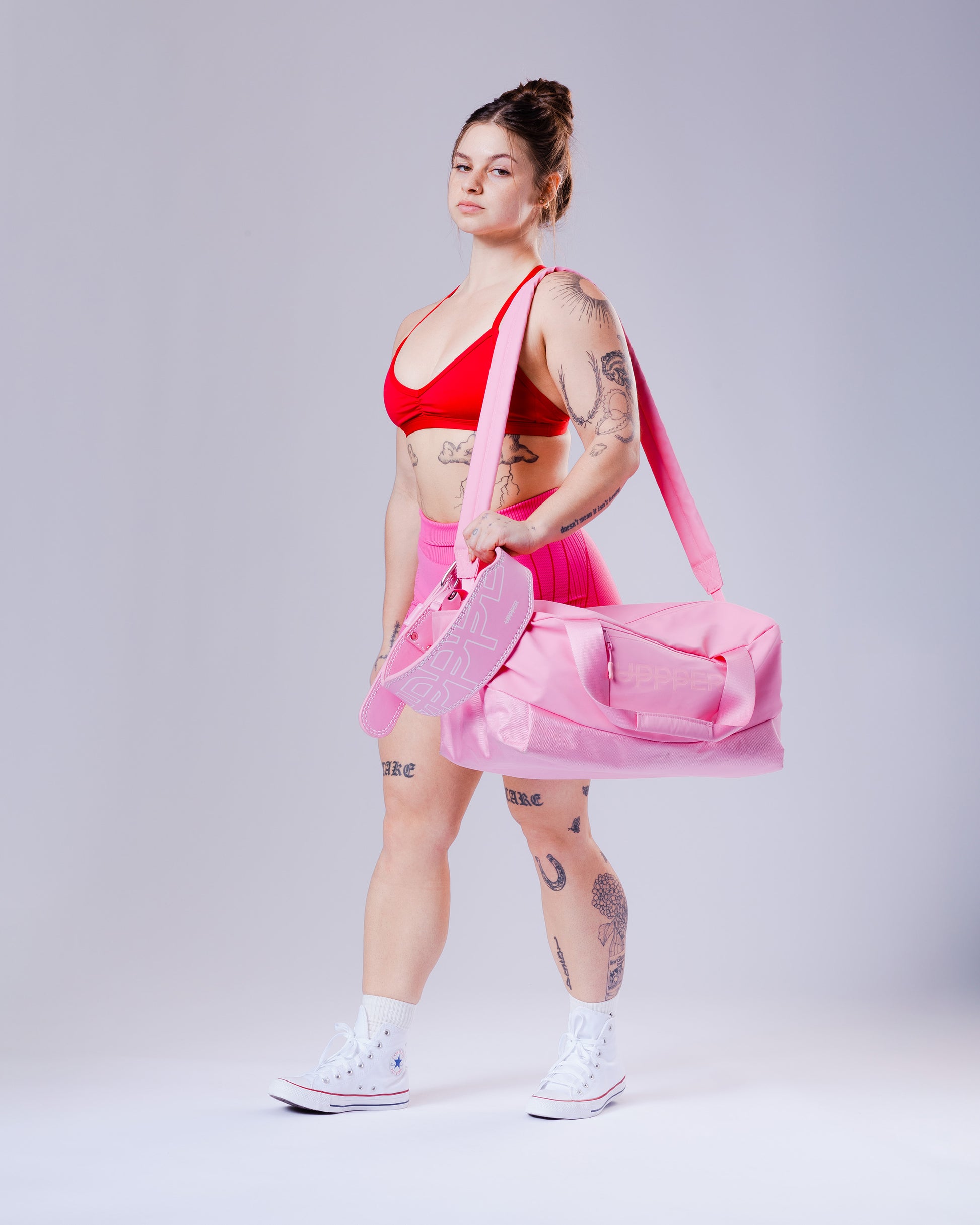 woman holding a pink uppper gym bag against a gray background